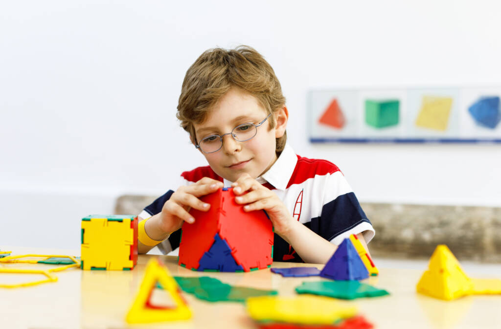 Happy kid boy with glasses having fun with building and creating geometric figures, learning mathematics and geometry