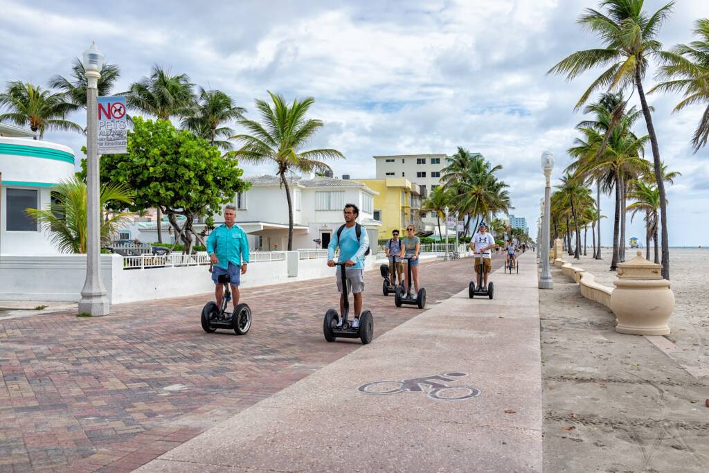 Hollywood, USA - August 4, 2021: North of Miami Beach, Hollywood broadwalk promenade in Florida and candid people riding segway scooters exploring with tour guide