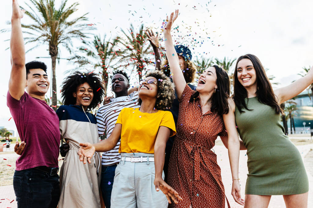 Młodzi ludzie bawią się na letnim przyjęciu - grupa młodych przyjaciół śmiejących się i świętujących razem podczas rzucania kolorowym konfetti podczas weekendowej imprezy na świeżym powietrzu